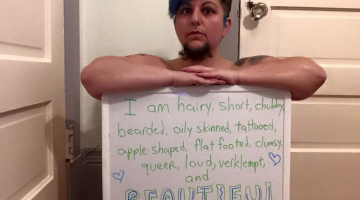 The author sits with a sign. The sign reads, "I am hairy, short, chubby, bearded, oily skinned, tattooed, apple shaped, flat footed, clumsy, queer, loud, verklempt, and BEAUTIFUL."