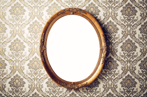 A brass vintage mirror hangs on a wallpapered wall