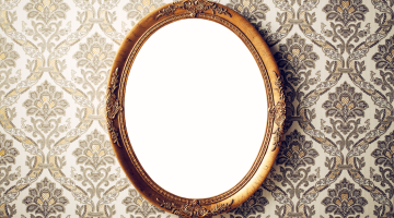 A brass vintage mirror hangs on a wallpapered wall
