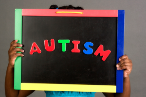 A young child holds up a chalkboard that reads "AUTISM" in colorful letters