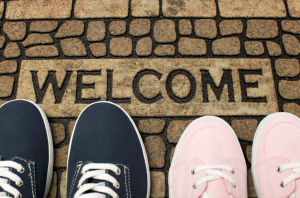 A pair of blue shoes and a pair of pink shoes are resting against a welcome mat