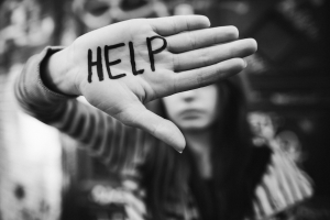 Young person covering their face with their hand; their hand has "HELP" written on it