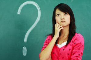 Person looking pensive, with a question mark drawn on a green chalk board behind them
