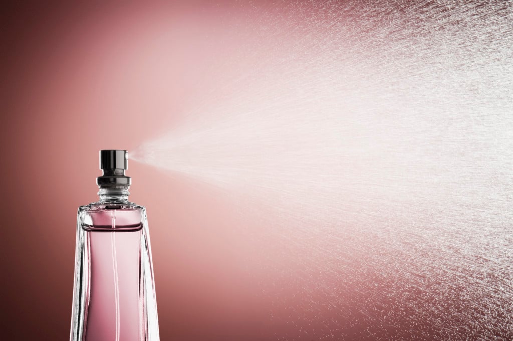 Glass bottle of pink perfume spraying a fine mist against a pink background