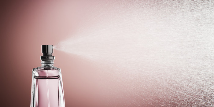 Glass bottle of pink perfume spraying a fine mist against a pink background