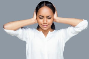Feeling tired and stressed, a frustrated young person covering ears with hands and keeping eyes closed while standing against gray background