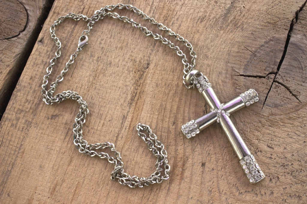 Silver Christian cross with small diamonds on wooden background
