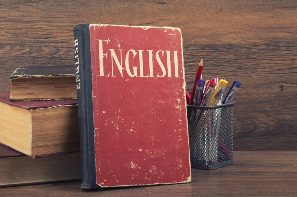 A book that reads "English" leans against a wooden background amidst school supplies