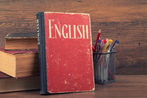A book that reads "English" leans against a wooden background amidst school supplies