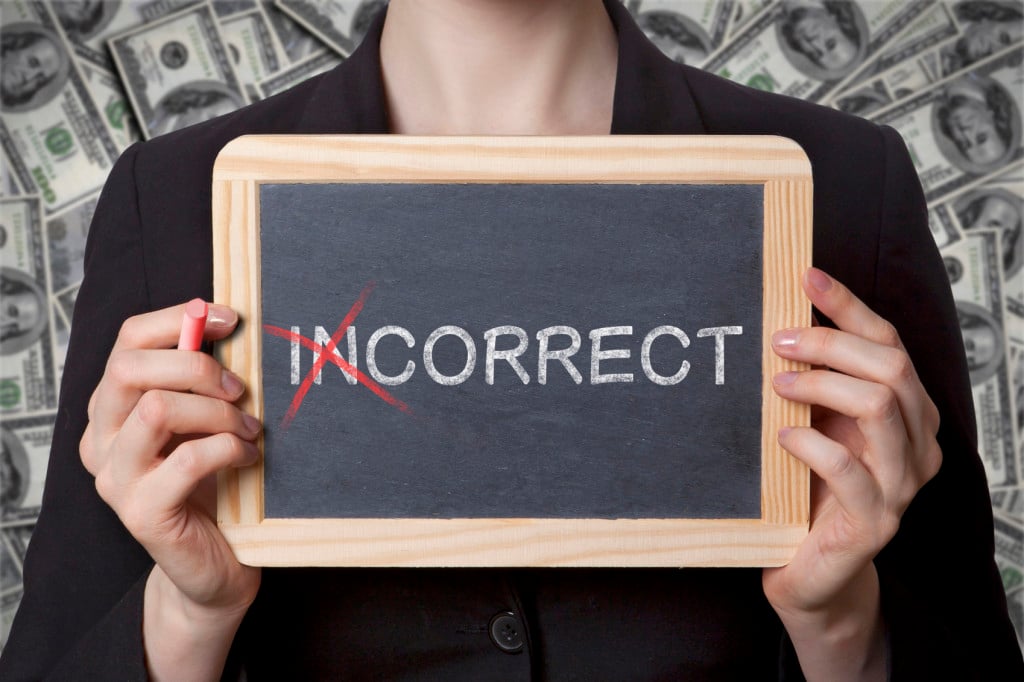 A person, against a background of money, holds up a chalkboard that says "Incorrect" with the "in" crossed out