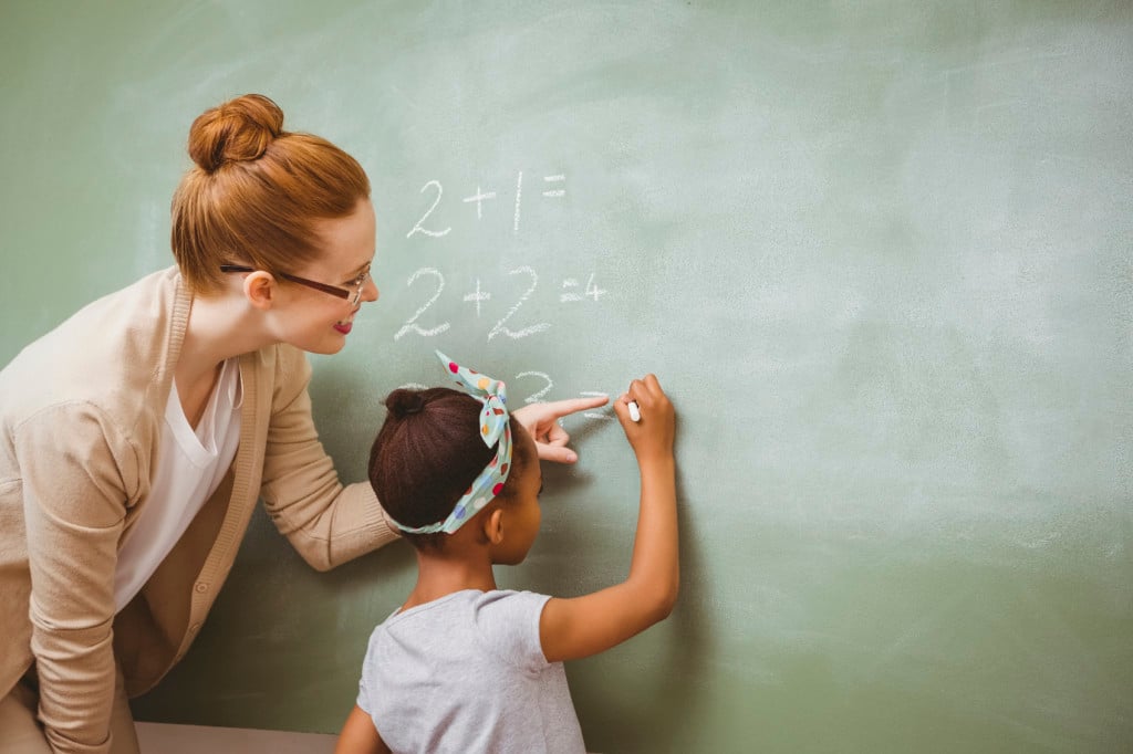 A teacher helping a young child with math at the chalkboard
