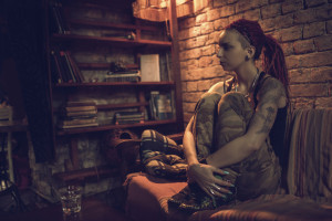 Young pensive person with dreadlocks sitting on sofa at home and looking away