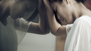 A person leans their head against a pane of glass in sadness and frustration.