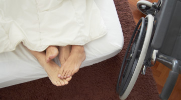 Two people in a bed, cuddling; an empty wheelchair sits beside the bed
