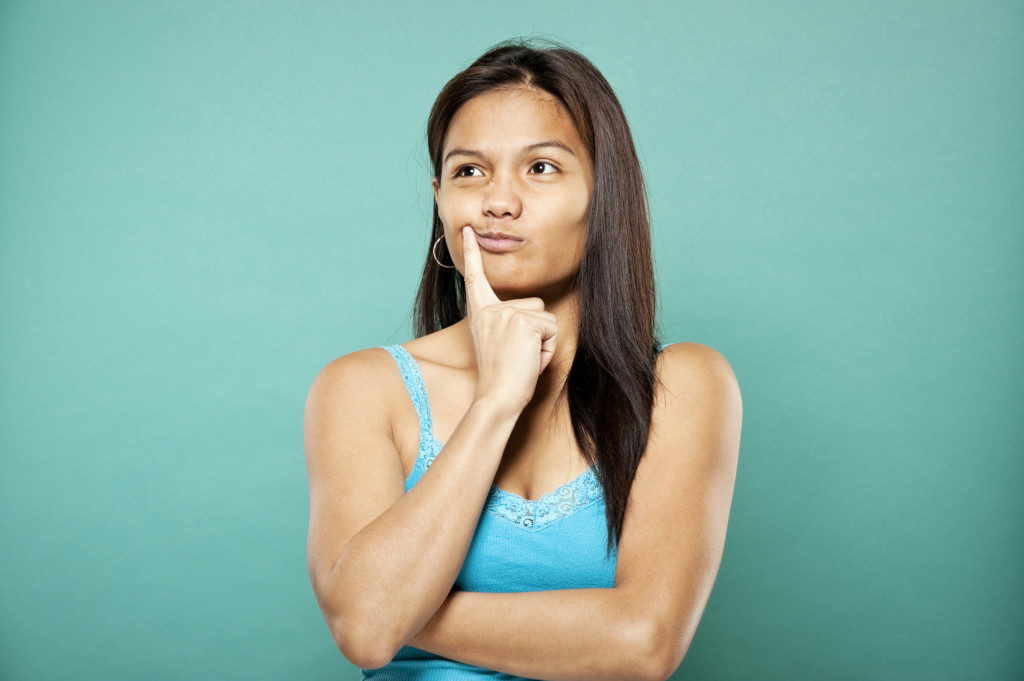 Person against a teal background with one hand against their face in thought