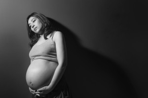 Pregnant person stands against a wall, looking worried or upset