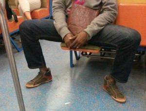 A person sitting on the subway has their legs spread wide, taking up more space than necessary