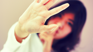 Person with one hand to their lips, signaling "shhh," and one hand in front of them, signaling "stop."