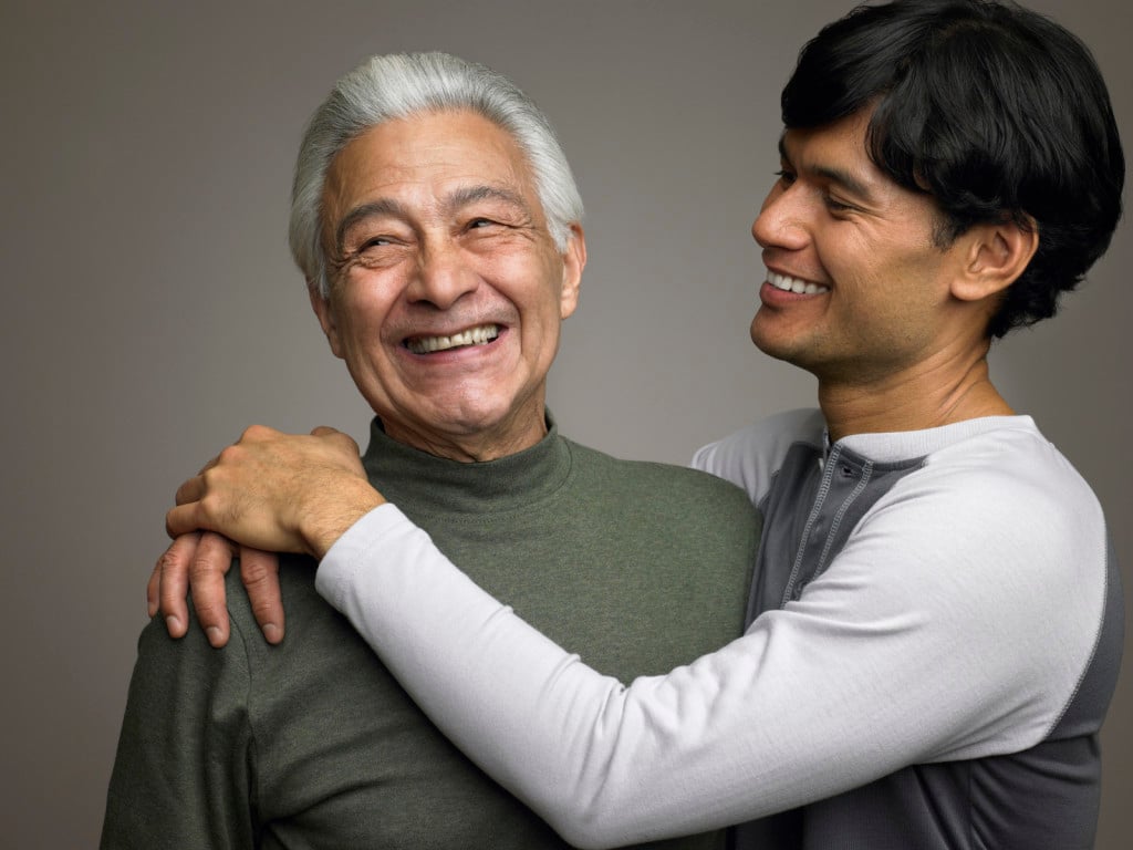 A younger person and an older person are hugging and smiling