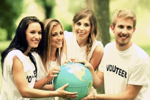 A group of four people, each wearing white t-shirts with "volunteer" written on them in black, hold a globe