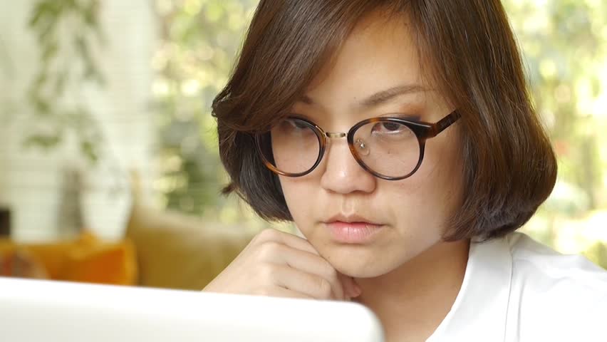 Young person in glasses, looking at their computer in contemplation