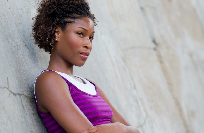 A person leaning against a wall with their arms crossed, in thought