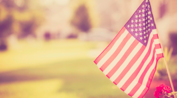 An American flag is pictured, sitting in a flower pot outside of a suburban home