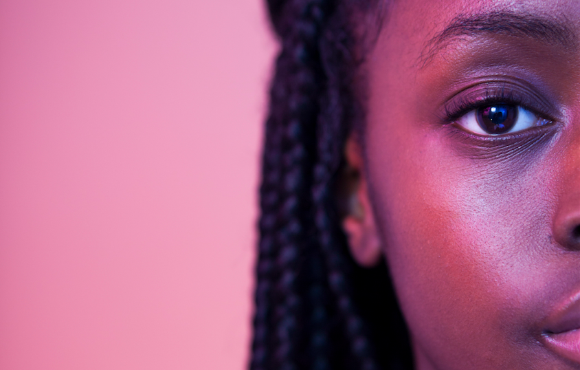 Under pink lighting, a young person stares deeply at the camera