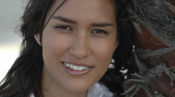 Young person leaning against a palm tree, smiling