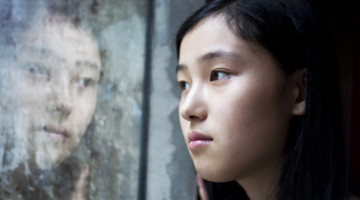 Young person, looking out a window at the rain, sad