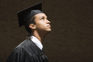 A college graduate in their cap and gown, looking skyward