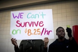 A person holding up a sign that reads, "We can't survive on $8.25/hr."