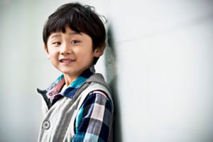 A young child, smiling happily while leaning against a white wall