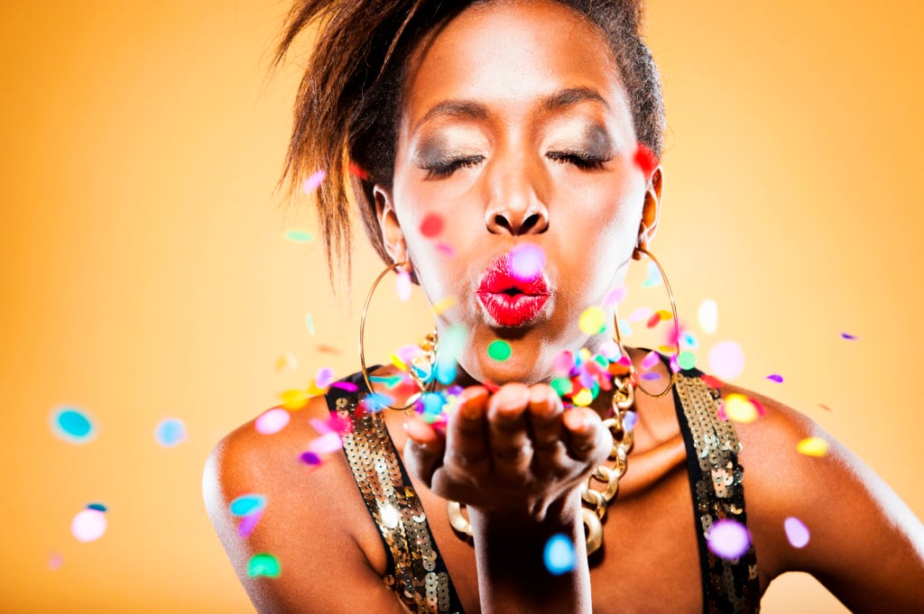 Person against a golden background, blowing colorful confetti