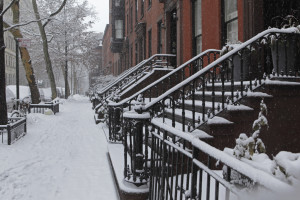 Snow covered Brooklyn brownstone townhouse stoops and sidewalk in winter. Snow is falling during a late winter storm in the Brooklyn Heights Historic District. Gardens, stoops, and sidewalks are covered in deep snow. Selective focus on the stoop steps.