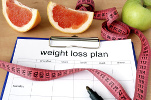 A clipboard that reads "Weight loss plan," surrounded by grapefruit slices, apple slices, and measuring tape