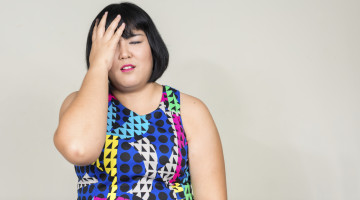 A brightly dressed person with a short bob is holding their head