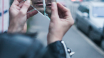 A person holds up broken glass to look at their reflection