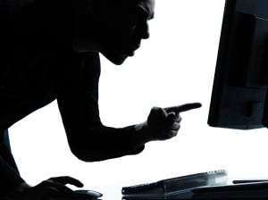 A silhouette of a person pointing angrily at their computer screen against a white backdrop.
