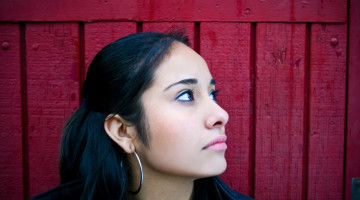 A person against a deep pink background, looking off to the side with a sad expression.