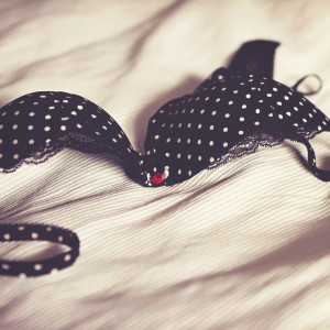 A black, polka-dotted lace bra on a bed.
