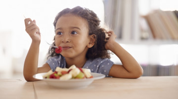 A small child is eating fruit salad.