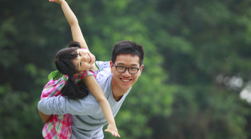 A child is being carried on someone's back, stretching their arms out and smiling.
