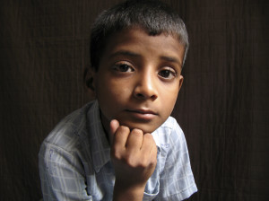 A young child looks pensively into the camera, their head resting on their fist.