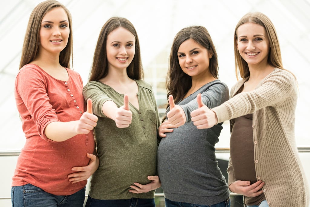 Portrait of four happy pregnant women are looking at the camera.