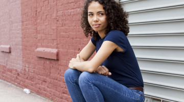 A person sits against a brick wall, staring off to the side.