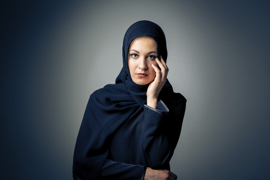 A person wearing hijab looks straight on into the camera, appearing skeptical, their hand touching their face.