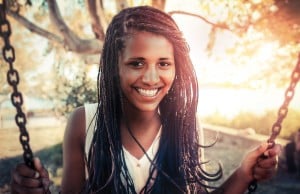 A person with long braids is smiling and holding two chains, leaning back into a swing.