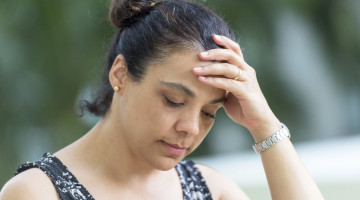 A person with an exhausted facial expression has their hand to their forehead.