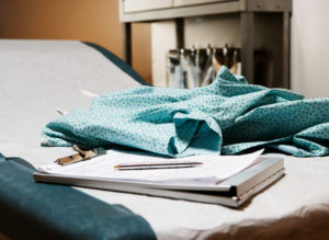 A medical gown laying on top of a medical exam table with clipboard and doctor's notes.